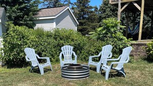 Un jardin avec un foyer et quatre fauteuils Adirondack disposés autour.