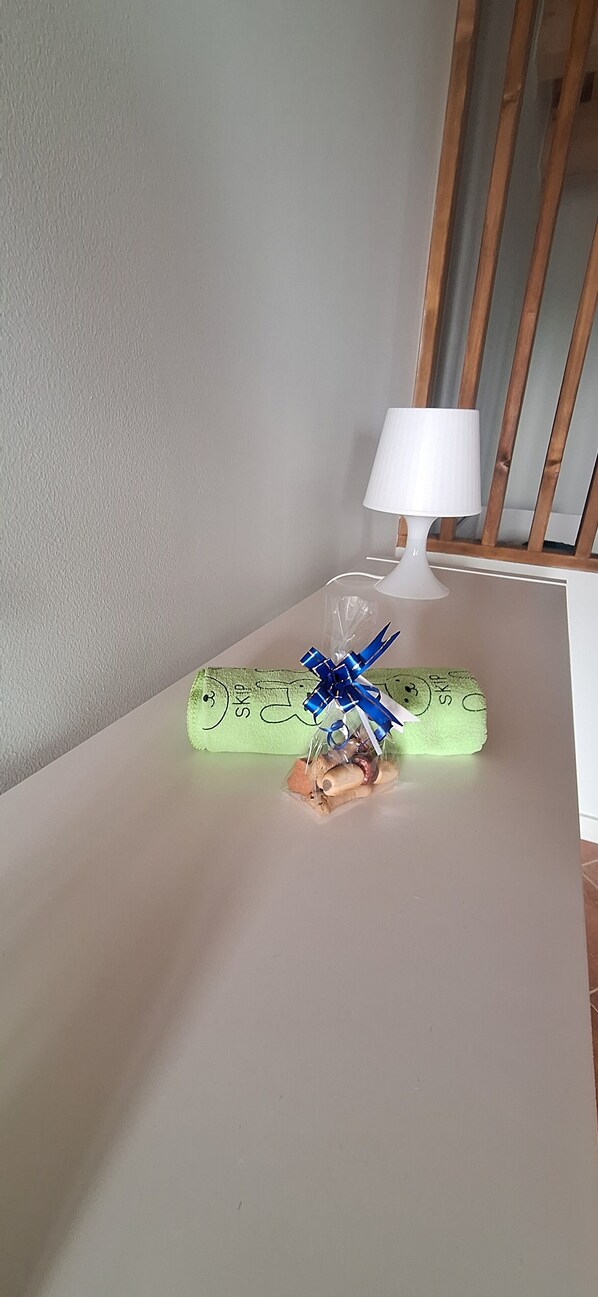 A white table with a green cylindrical object wrapped in plastic, a white lamp, and wooden slats in the background.