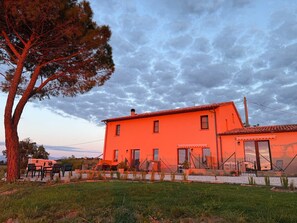 A two-story building with a red exterior, a fenced yard, and a tree to the left. - App. Salvia @ Casa Talènt, vacation in the heart of Le Marche! Dogs welcome! (Marche)