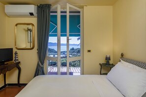 A hotel room with a bed, a TV, a lamp, a small table, and a view of the sea through a door. - Orizzonte Blu With Terrace by Wonderful Italy (Santa Margherita Ligure)