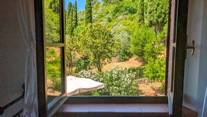 Una habitación con un ventanal grande que ofrece vistas a un jardín con árboles y una mesa blanca.