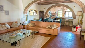 Una sala de estar con un sofá, una mesa de centro de vidrio y una cocina visible a través de un arco.