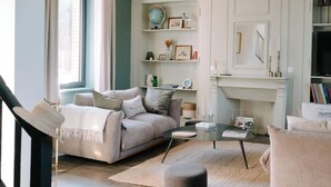 A living room with a sofa, ottoman, and coffee table, a fireplace, and a bookshelf with various items. - Maison Eudoise, swimming pool and spa (Eu)