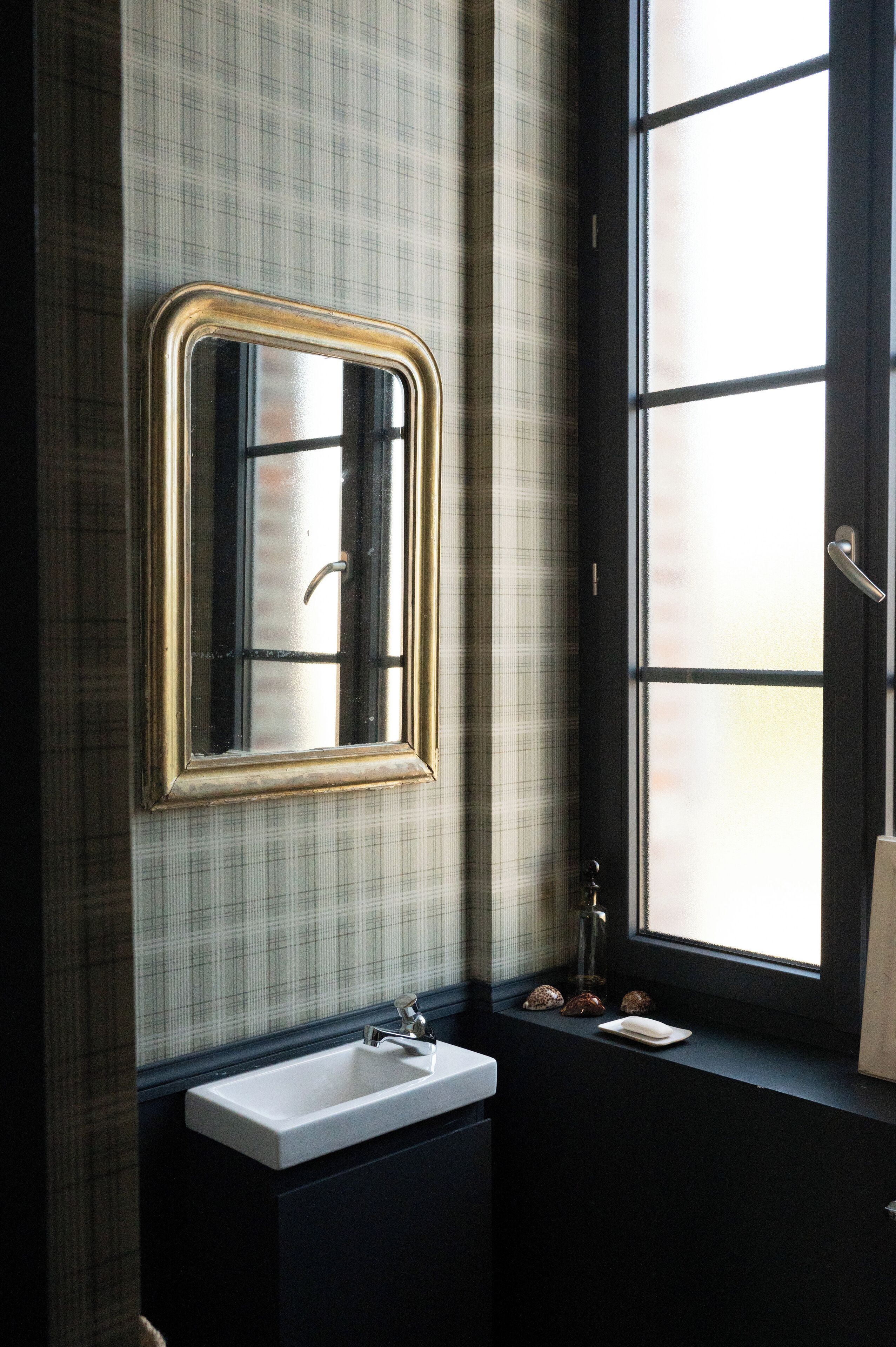 A bathroom with a large mirror, a sink, and a window with frosted glass.