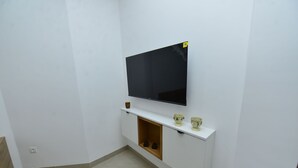 A white room with a mounted TV, a small shelf with two cups, and a wooden cabinet with shoes. - Luxury Sea View Apartment in El Maamoura, Tunisia (El Maamoura)