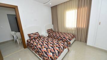 A modern bedroom with a large bed, a bedside table, a chair, and a window with curtains.