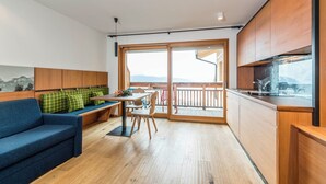 A modern kitchen with wooden cabinets, a dining area with a bench, and a view of mountains through large glass doors. - Pension Haus Tirol - Lausbua (Tschöfas)