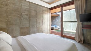 A modern hotel room with a large bed, a TV mounted on the wall, and a sliding glass door leading to an outdoor area. - Aqilah Villa (Legian)