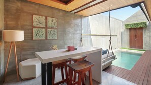 A modern outdoor kitchen with a bar area, wooden stools, and a pool. - Aqilah Villa (Legian)