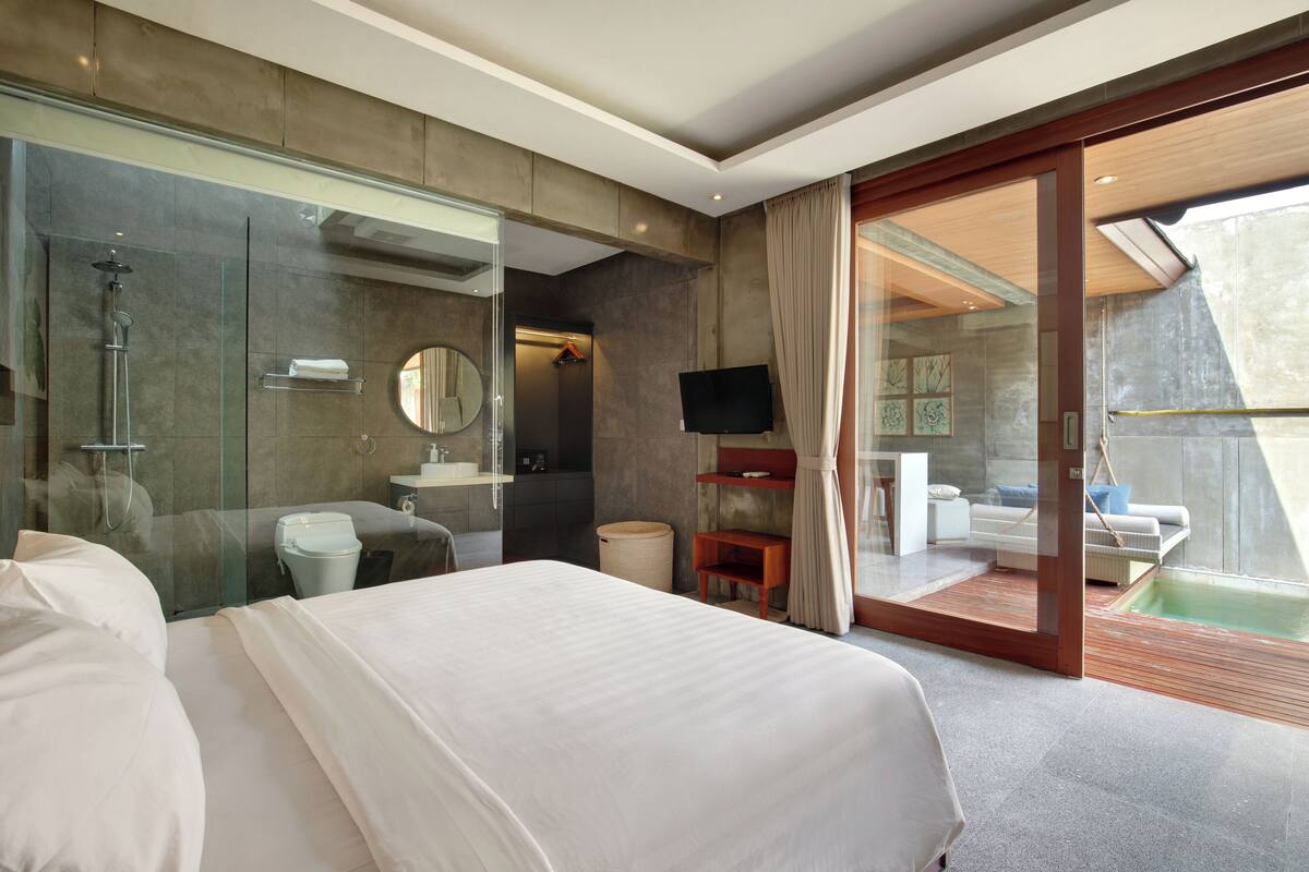 A modern hotel room with a large bed, a glass-enclosed shower, a television, and a balcony with a pool.