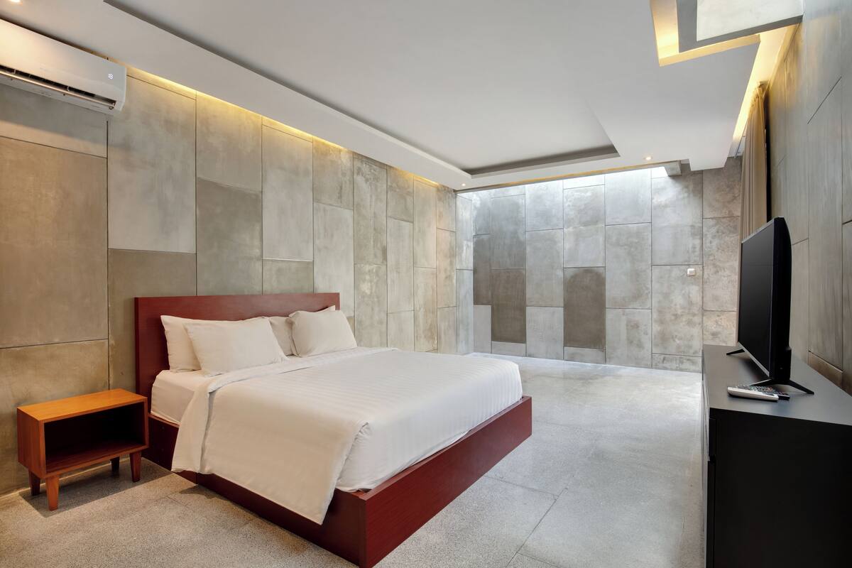 A modern bedroom with a large bed, a wooden nightstand, a flat-screen TV, and a stone wall.