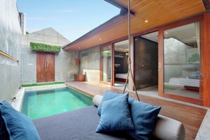 Un espace piscine extérieur moderne, doté d’une terrasse en bois, d’une balançoire et d’un coin salon avec des coussins.