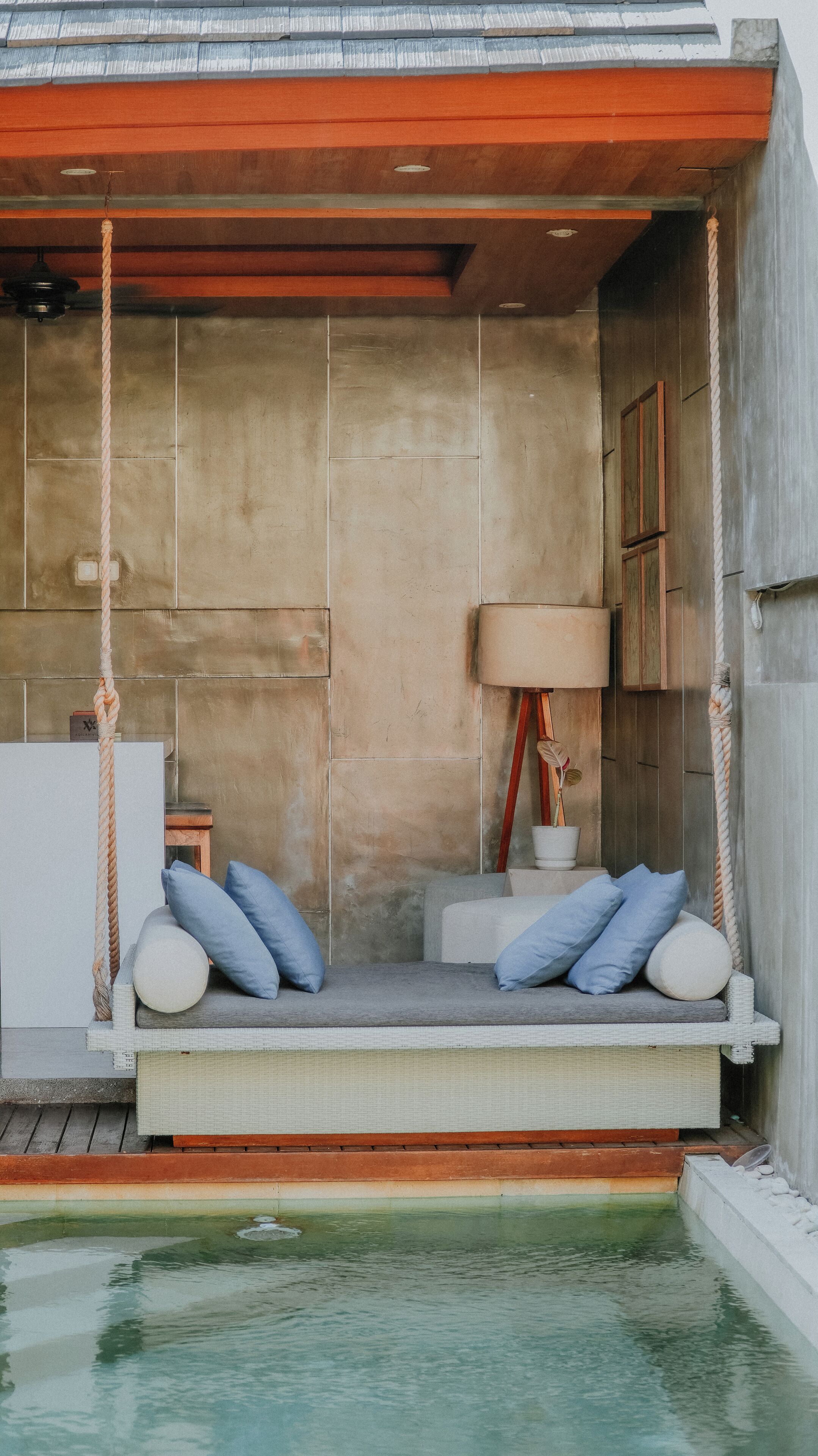 A modern outdoor seating area with a swing, a small table, and a lamp.