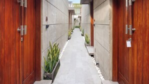 A corridor with wooden doors and a tiled floor, leading to a building with a modern design. - Aqilah Villa (Legian)