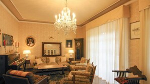 A classic living room with a chandelier, a sofa set, a coffee table, and a piano.