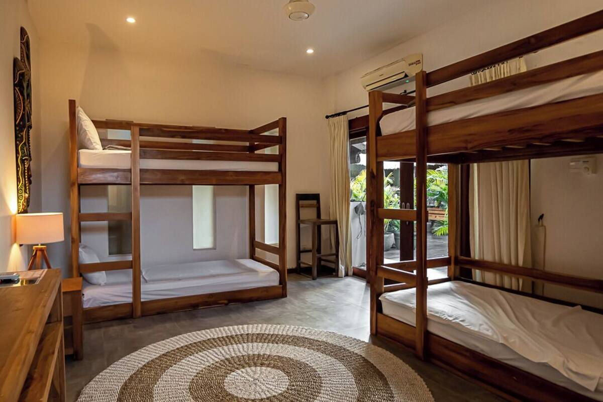 A room with two bunk beds, a wooden desk with a lamp, and a large woven rug.