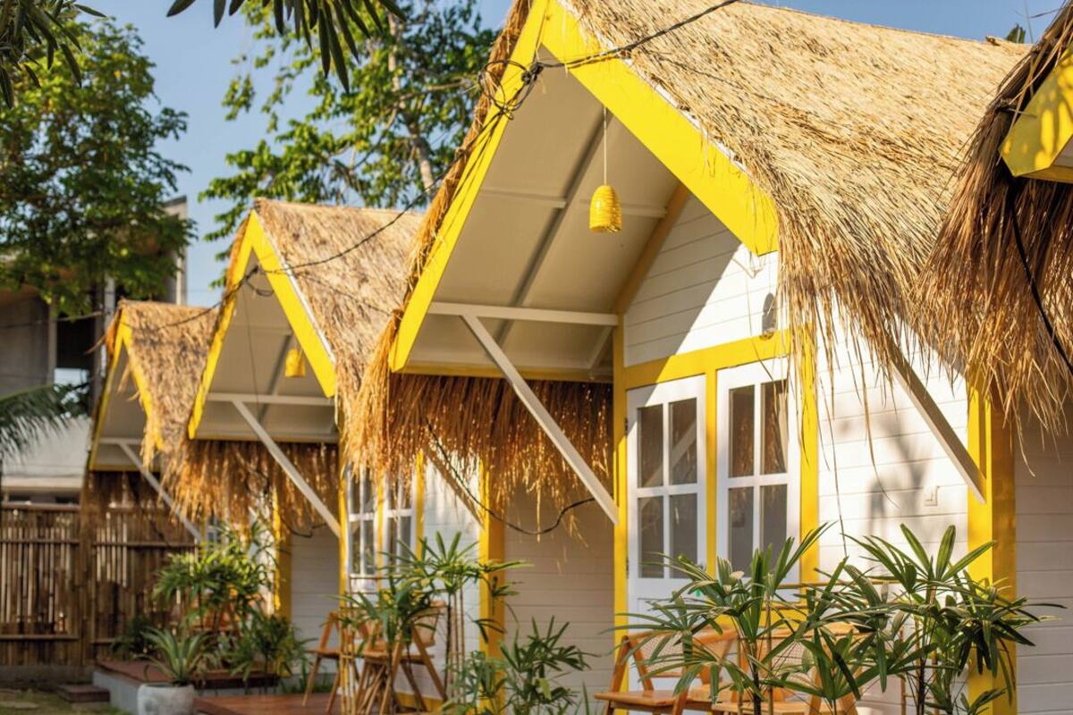 A row of yellow and white buildings with thatched roofs, surrounded by greenery.