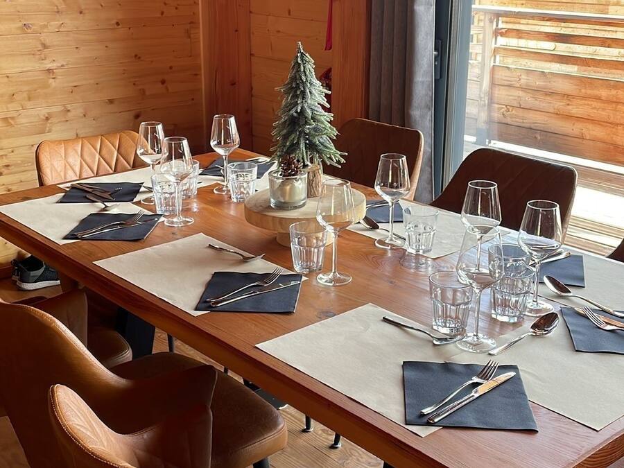 A dining table set for six with a small Christmas tree centerpiece, leather chairs, and a painting of a deer on the wall.