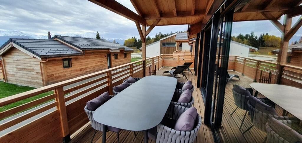 A wooden deck with a table and chairs, overlooking a mountainous landscape.