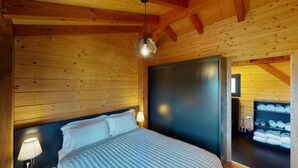 Un dormitorio de cabaña de madera con cama, mesitas de noche y armario.