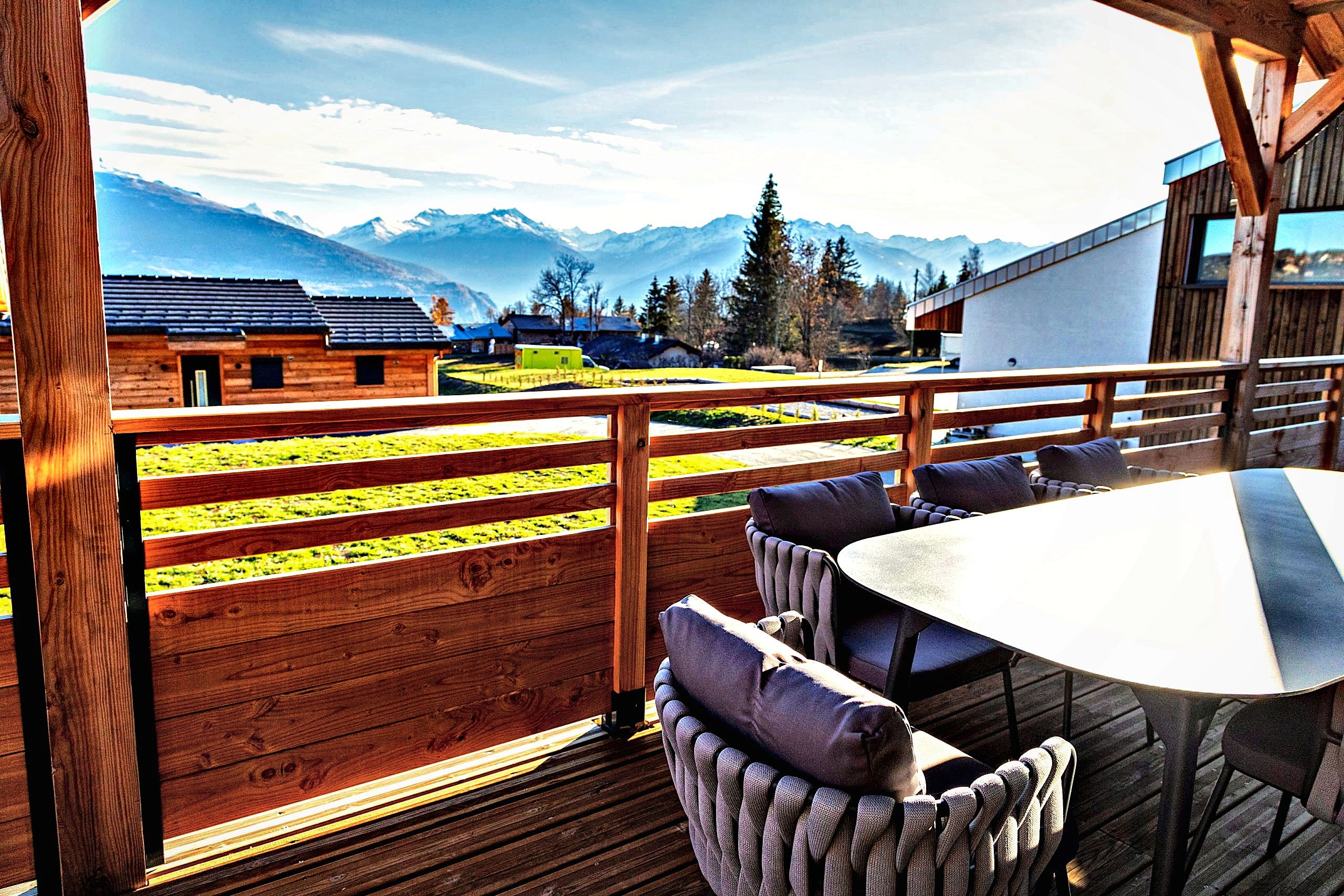 Una terraza de madera con una mesa y sillas, con vistas a un paisaje montañoso con edificios.