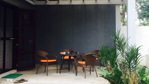 Un espacio de estar al aire libre cubierto con sillas de mimbre y una mesa, rodeado de follaje.