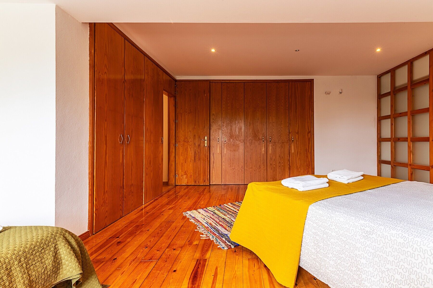 A bedroom with a bed, wooden wardrobe, and a small rug.