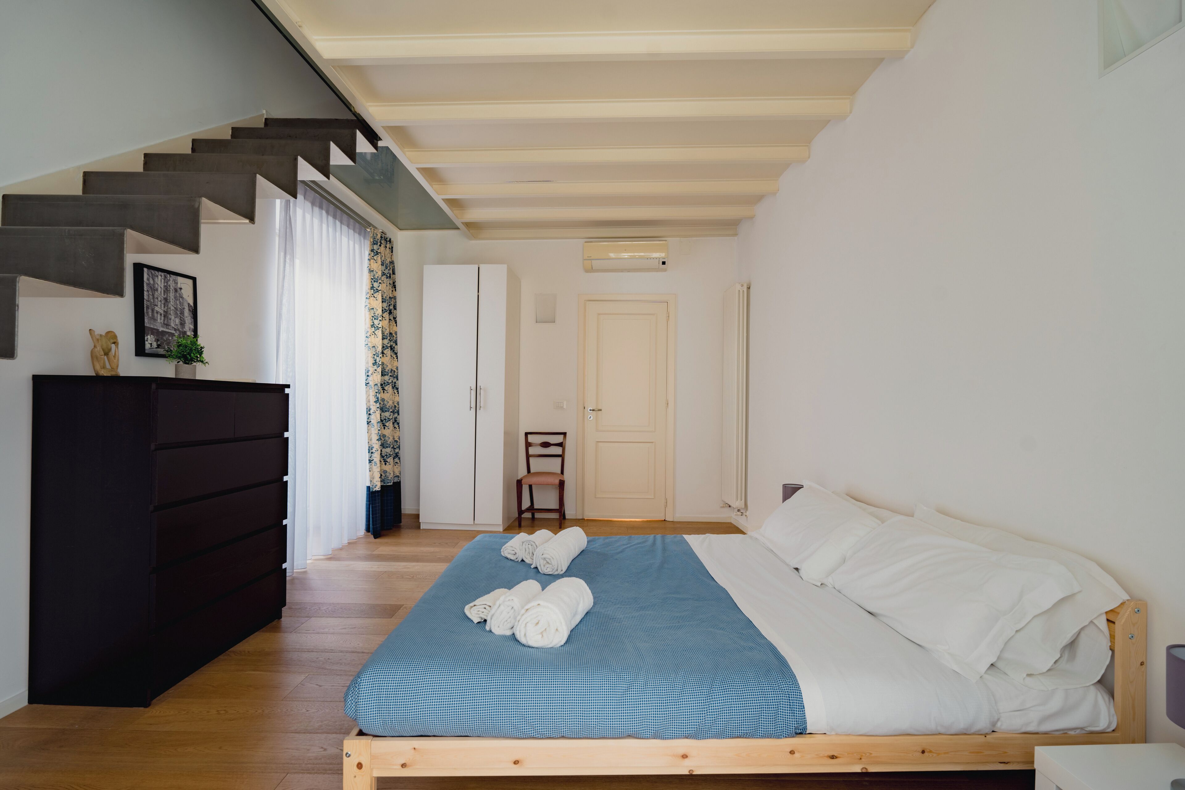 A bedroom with a wooden bed, a dark dresser, a staircase, and a door.