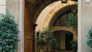 Une entrée en arc surmontée d’une porte en bois, agrémentée de plantes en pot et d’un chemin de pierre menant à une cour intérieure.