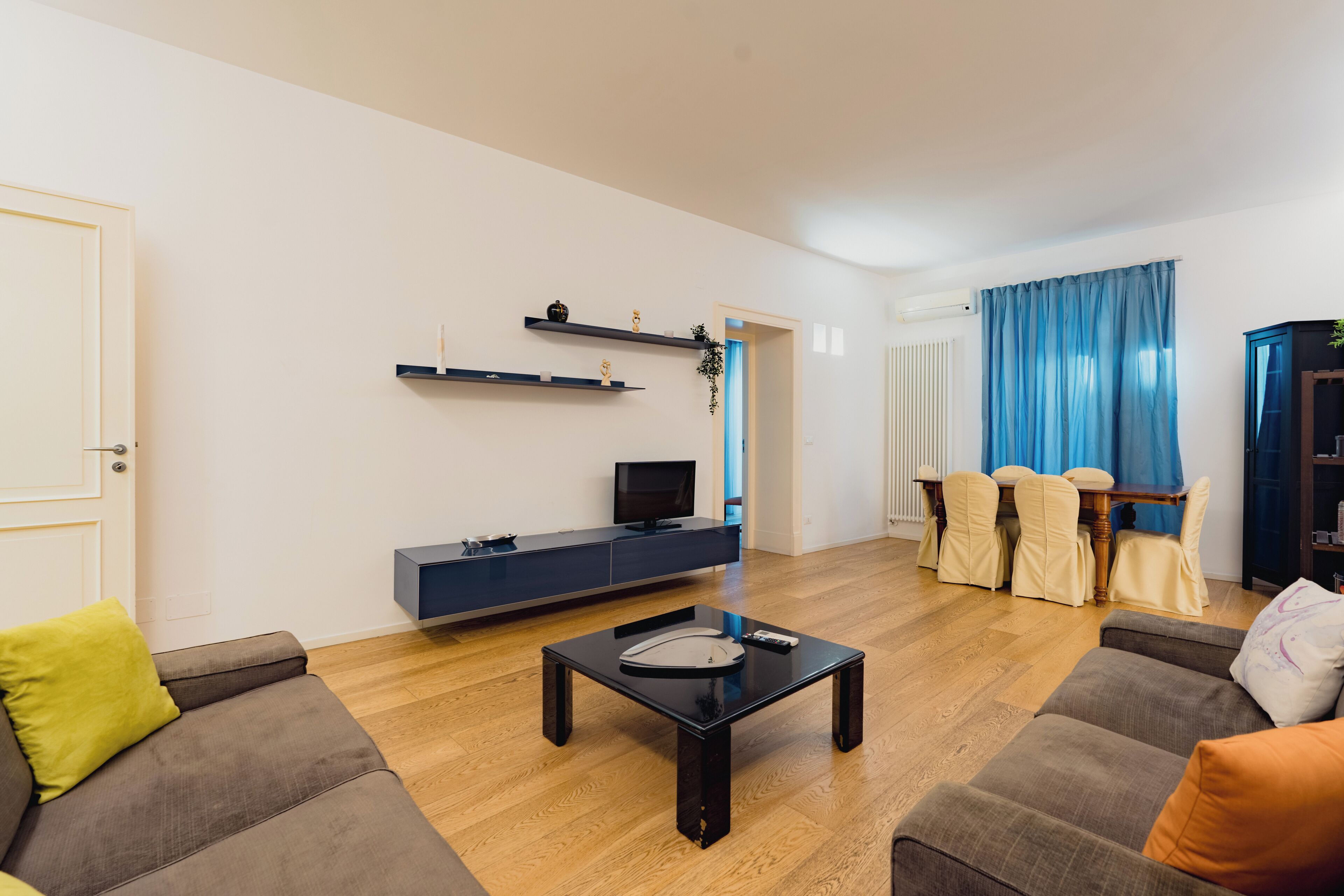 Ein modernes Wohnzimmer mit Sofa, Couchtisch, Fernseher auf einem Schrank und einem Essbereich mit Stühlen und Tisch.