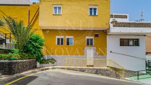 Un bâtiment jaune à deux étages, doté d’un balcon, d’un escalier et d’un petit jardin.