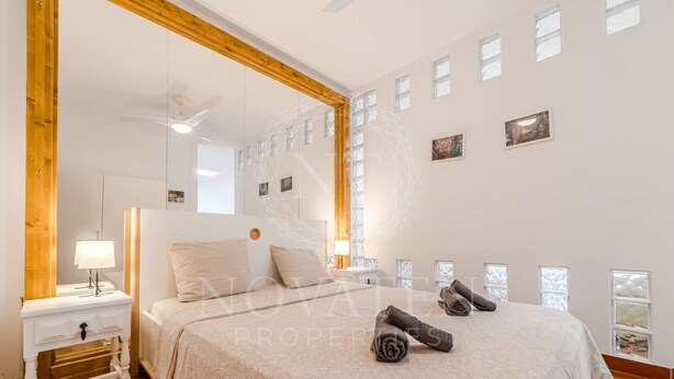 Une chambre à coucher avec un grand lit, une table de chevet, un miroir et un ventilateur de plafond.