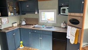 Una cocina compacta con armarios azul oscuro, una estufa a gas, un fregadero, un microondas y un refrigerador.