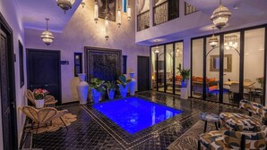 Un'area piscina interna di lusso, con una piscina blu, lampadari elaborati e un design moderno.