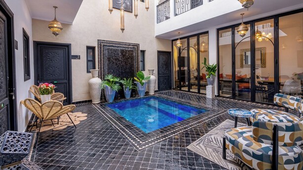 Un'area piscina con pavimento a scacchi bianco e nero, una piscina, mobili in vimini e luci a sospensione.