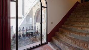 A staircase with a brick design leading to an upper floor, a glass door opening to a courtyard with a table and chairs, and a view of a building with a metal fence. - Wonderful  villa for 4 people with WIFI, A/C, TV and balcony (Mensano)