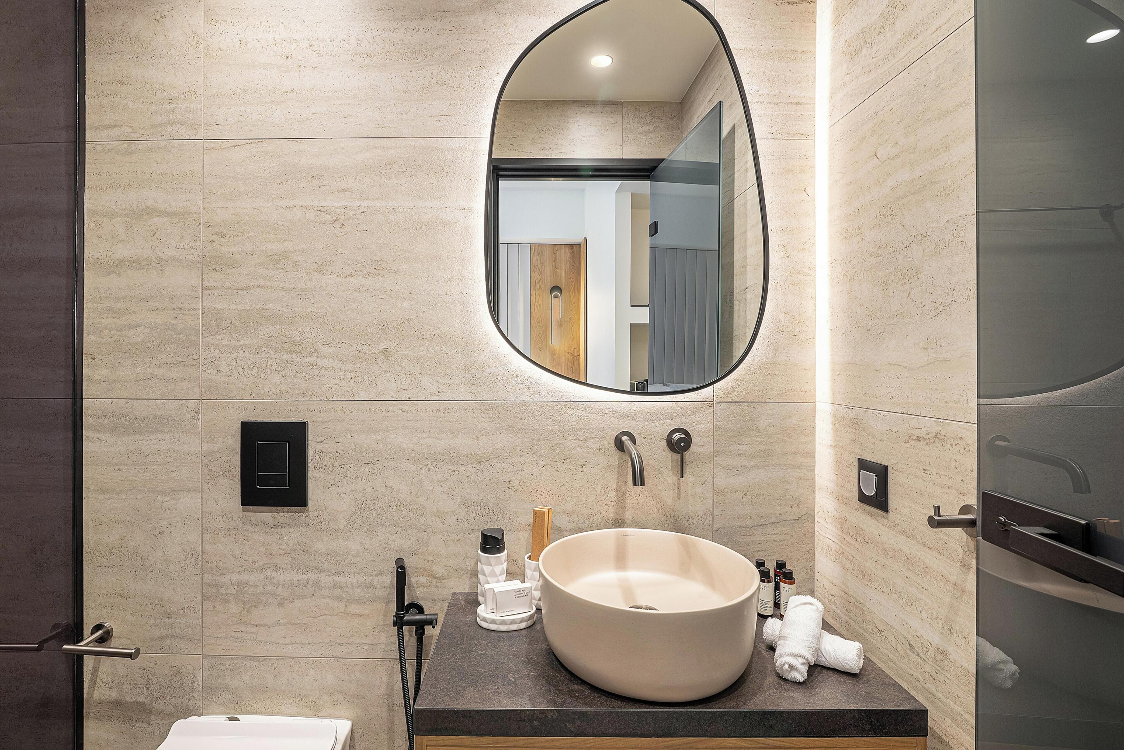 A modern bathroom with a large oval mirror, a round sink, and a towel rack.
