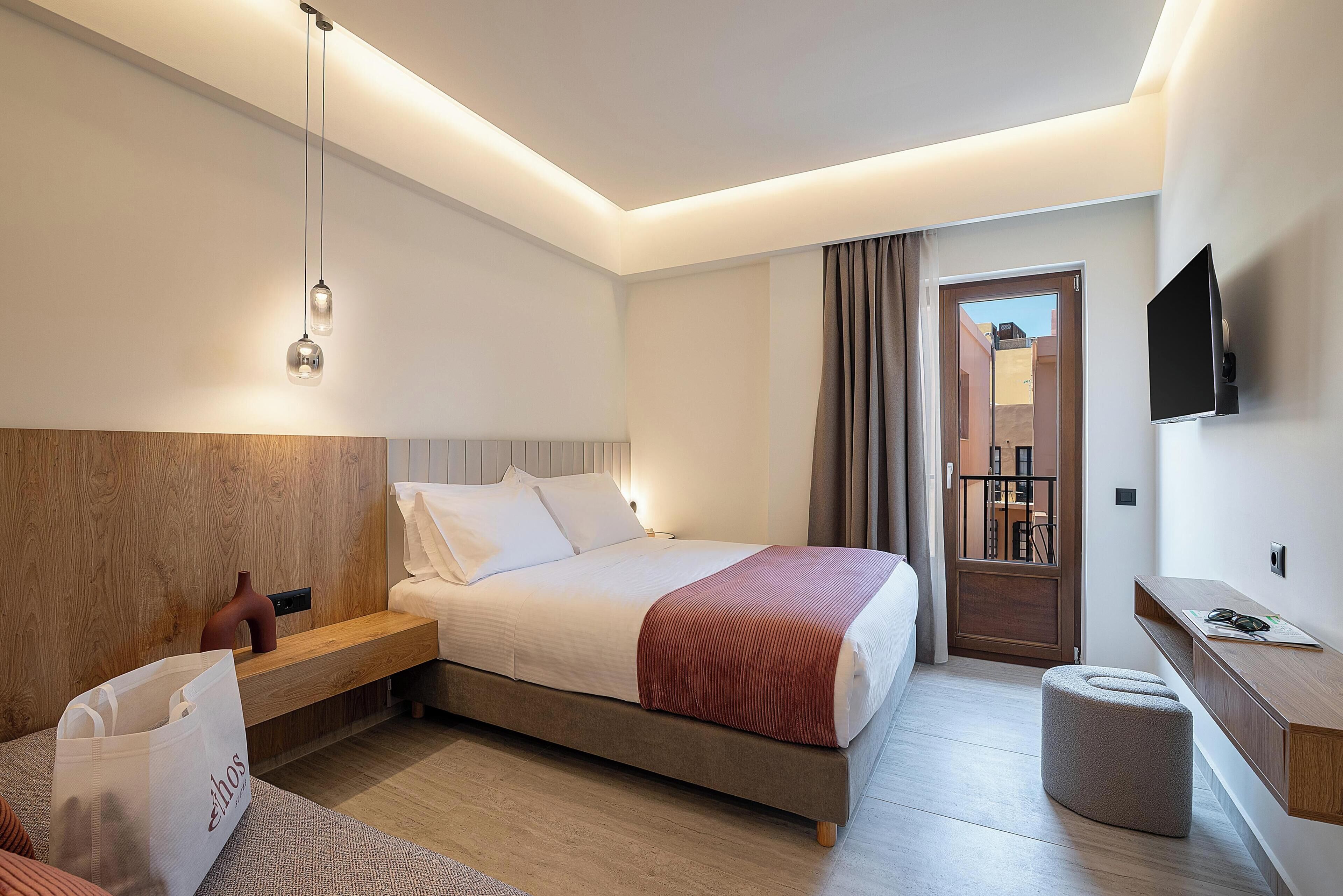 A modern hotel room with a bed, bedside table, TV, and a view of the outside.