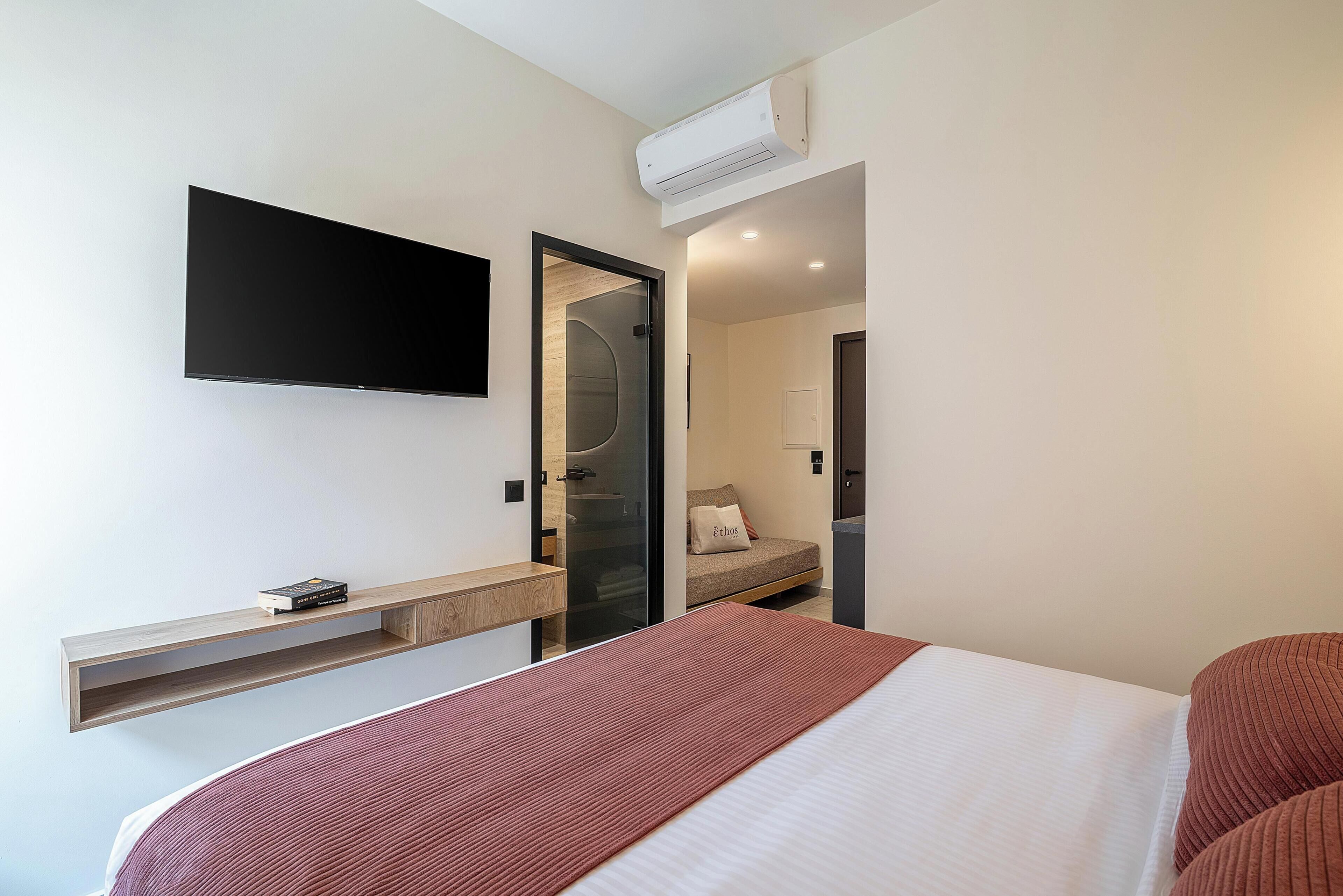 Une chambre d’hôtel moderne équipée d’un lit, d’un téléviseur fixé au mur, d’une étagère intégrée et d’une porte donnant accès à la salle de bain.