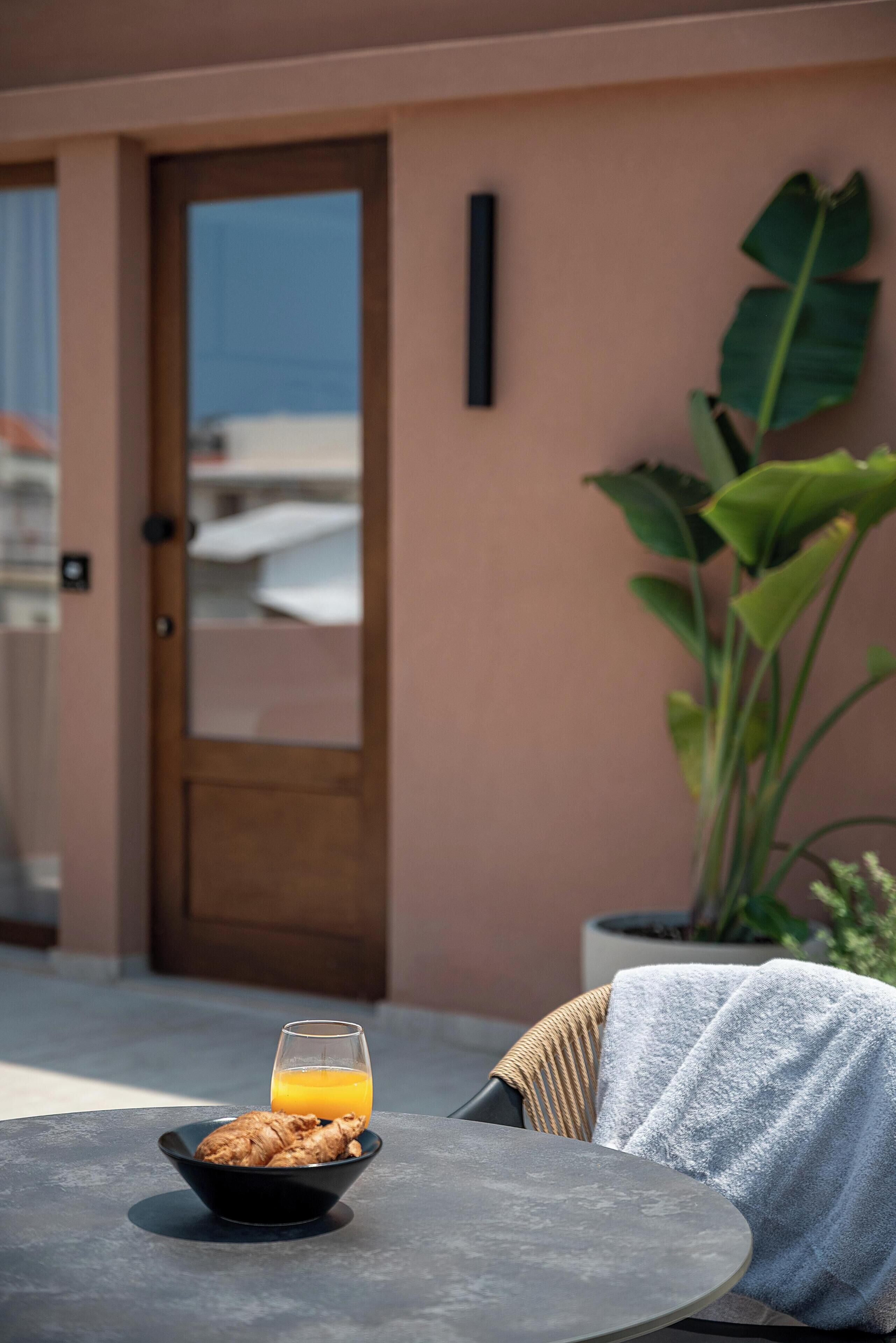 Ein Esstisch mit einer Schüssel Essen und einem Glas Orangensaft, ein Stuhl mit einem Handtuch sowie eine große Pflanze im Hintergrund.