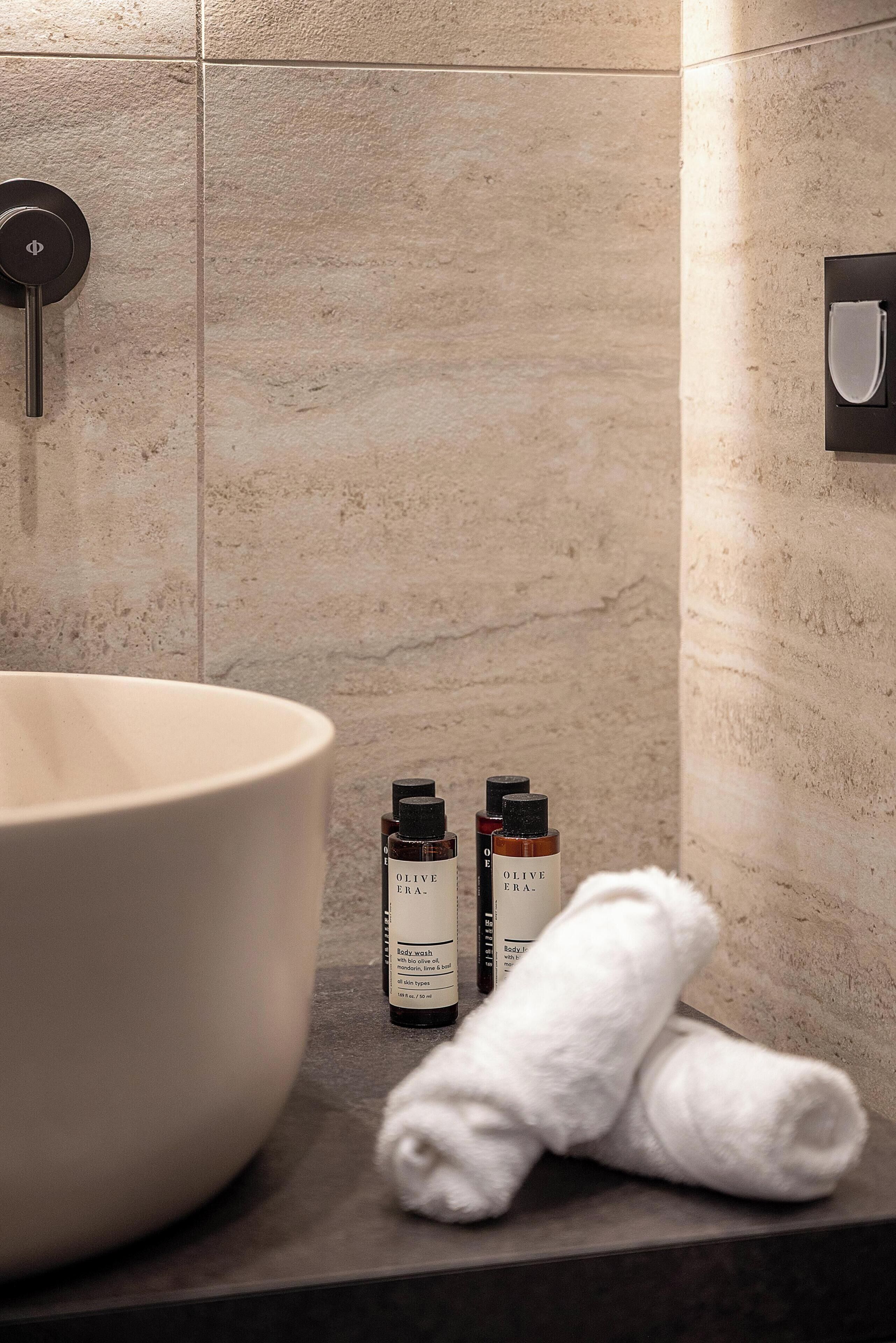 Un baño con un lavamanos grande, dos botellas de aceite de oliva y una toalla blanca sobre el mostrador.