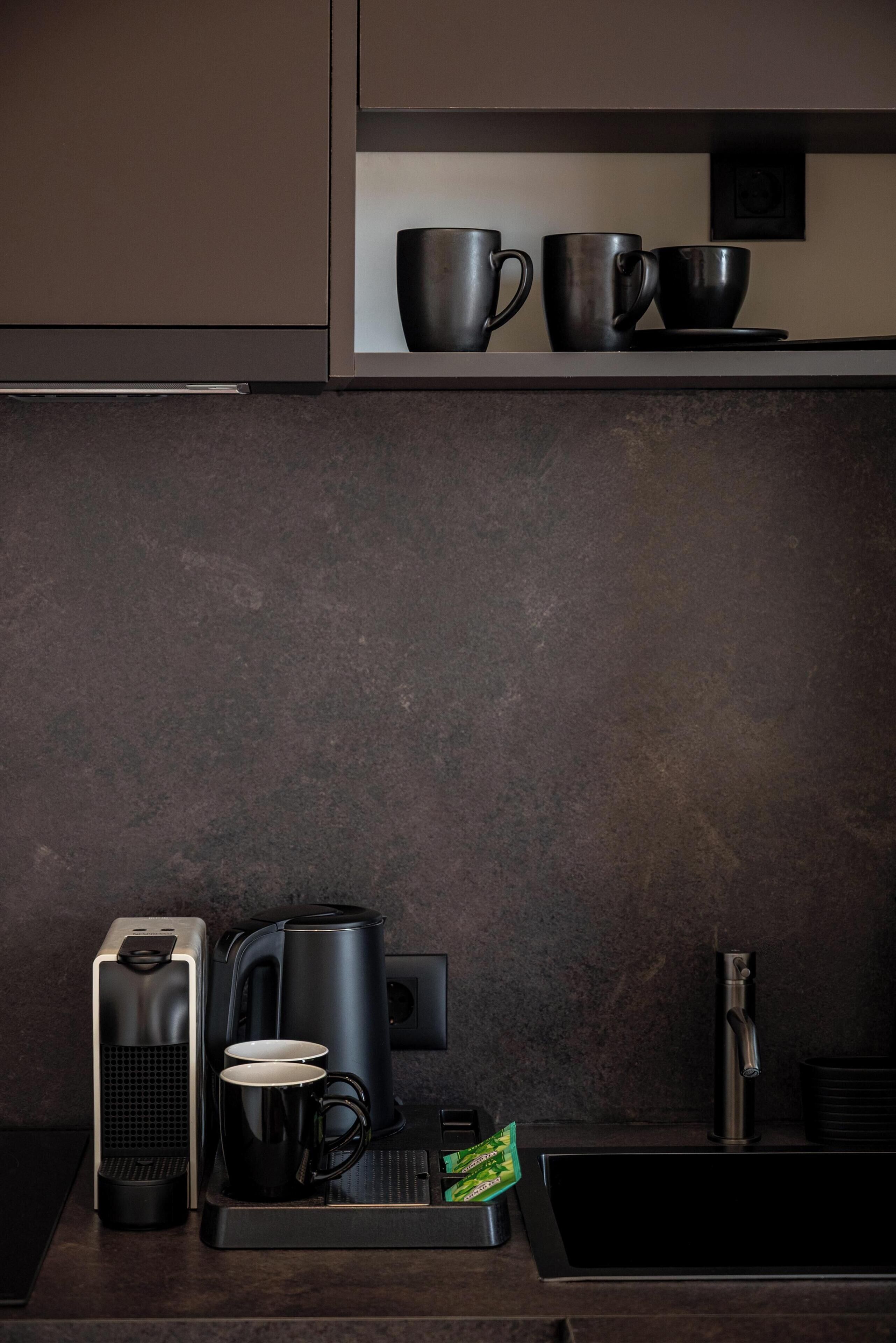 A modern kitchen with a coffee maker, two mugs, and a kettle on the counter.