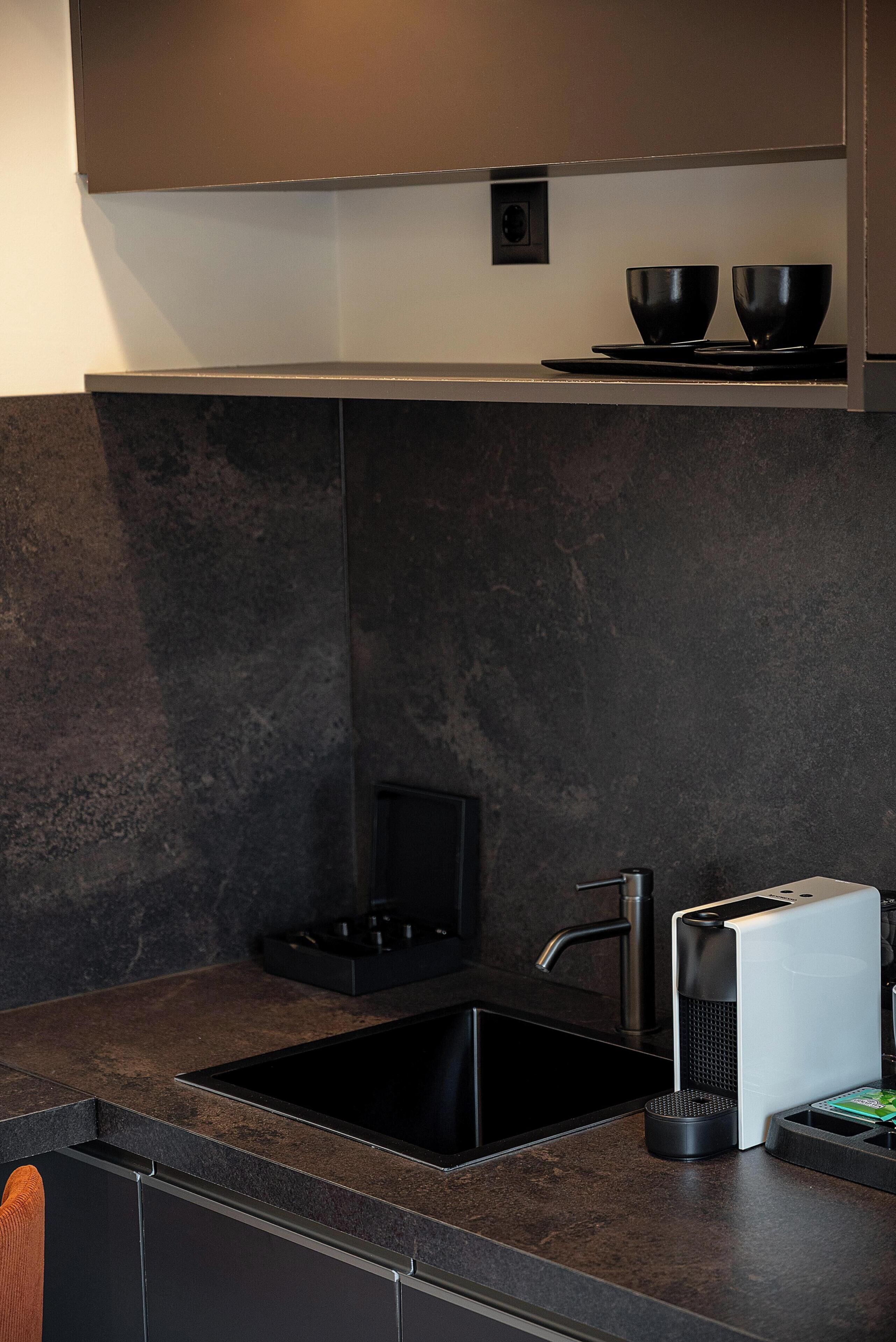 Una cocina moderna con encimera negra, un lavamanos de acero inoxidable y una campana extractora integrada.