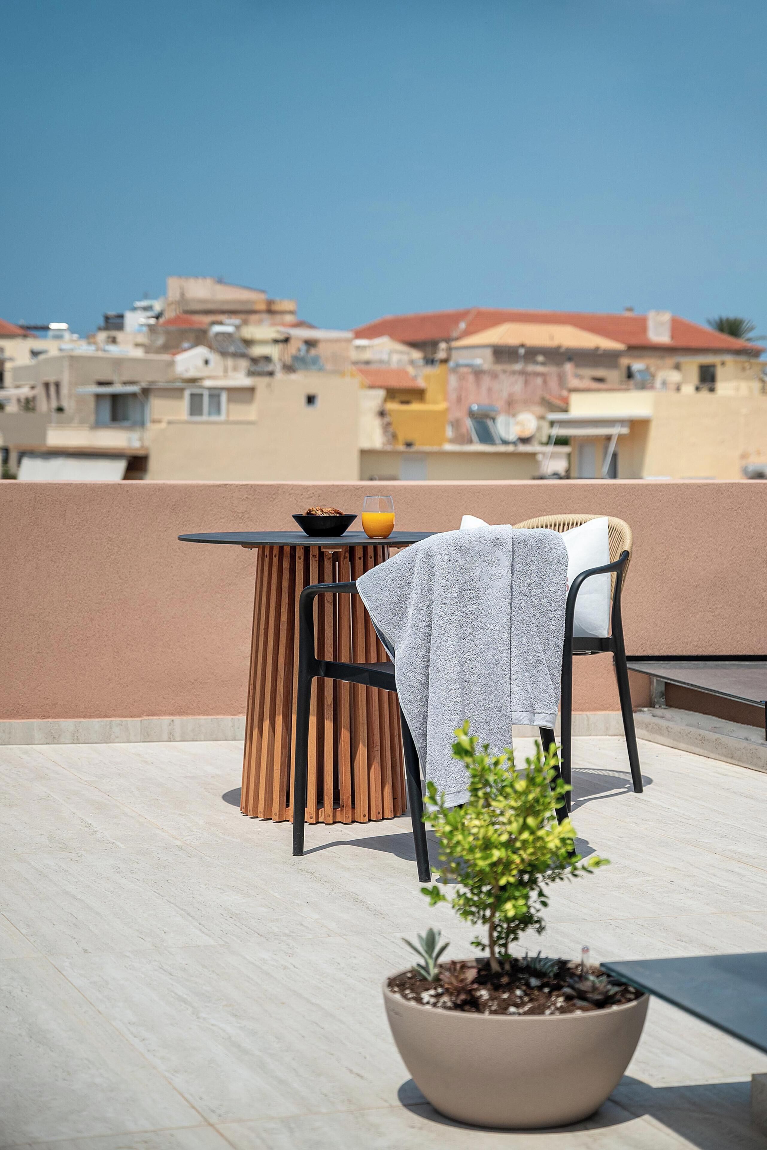 A terrace with a table, chairs, a potted plant, and a bowl of cereal with orange juice.