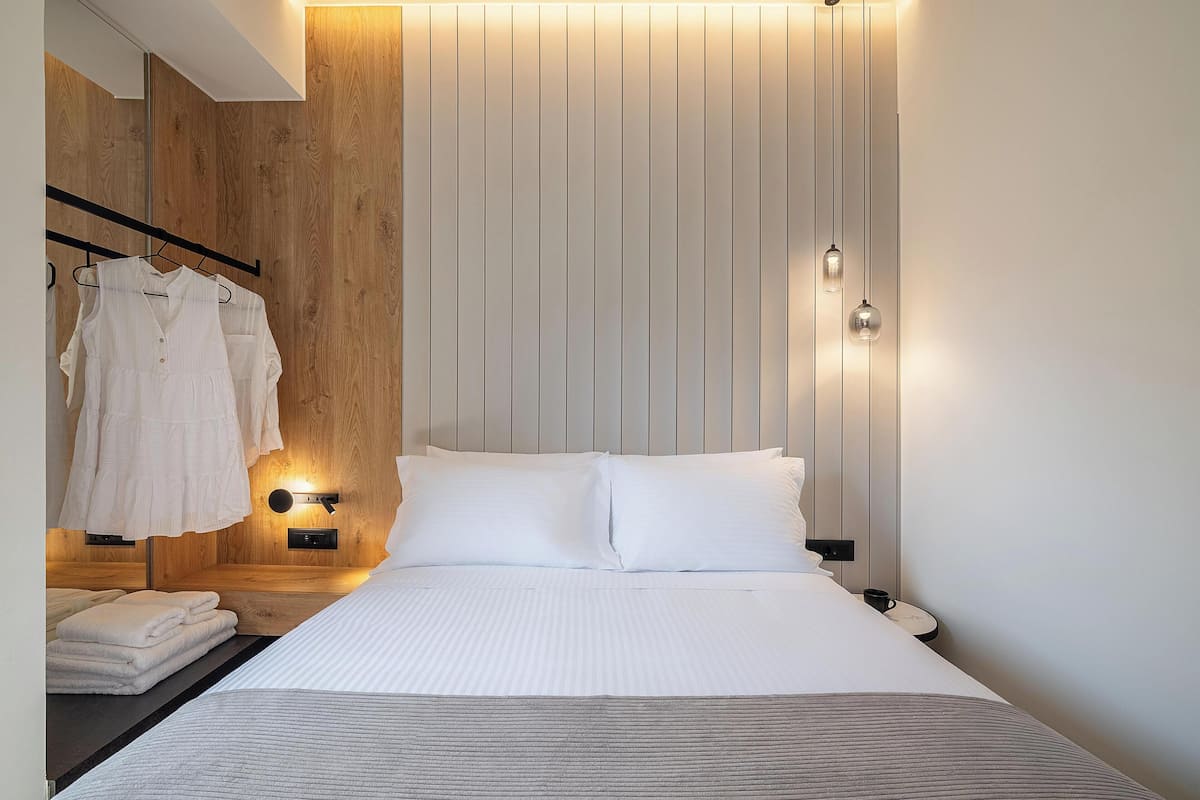 A modern hotel room with a large bed, a wooden wall, and a clothing rack with folded towels.