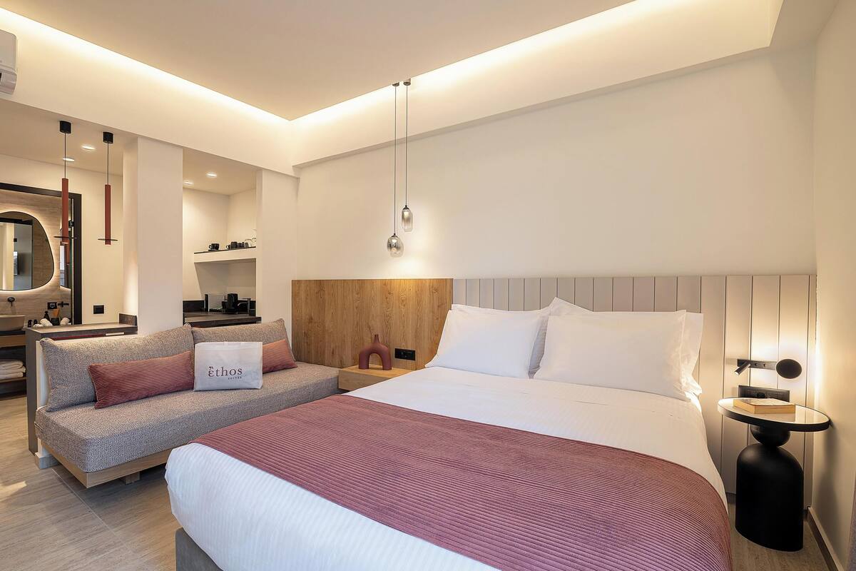 A modern hotel room with a large bed, a sofa, a bedside table, and a mirror.