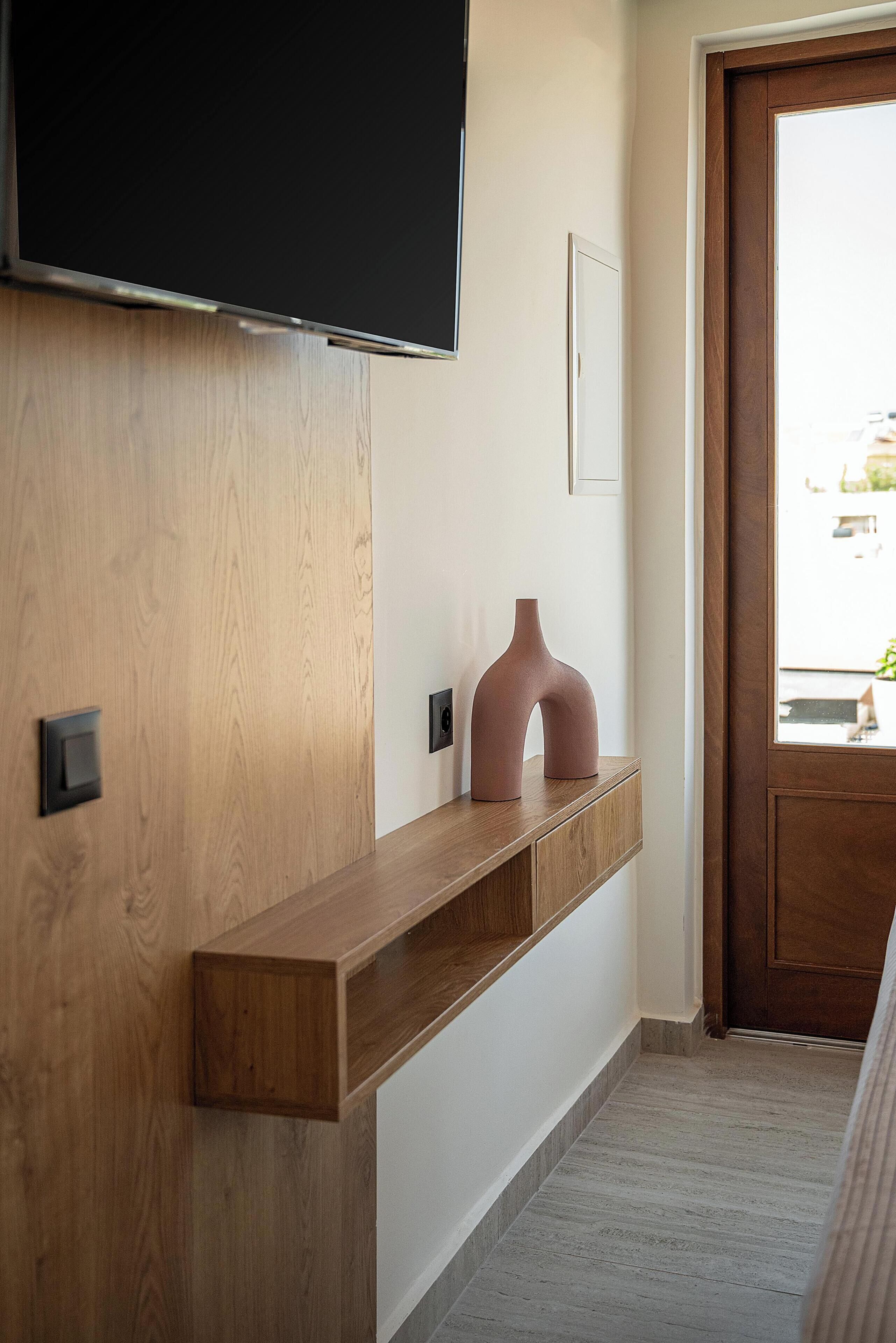 A modern room with a wooden wall, a mounted TV, a console table with a vase, and a door leading outside.