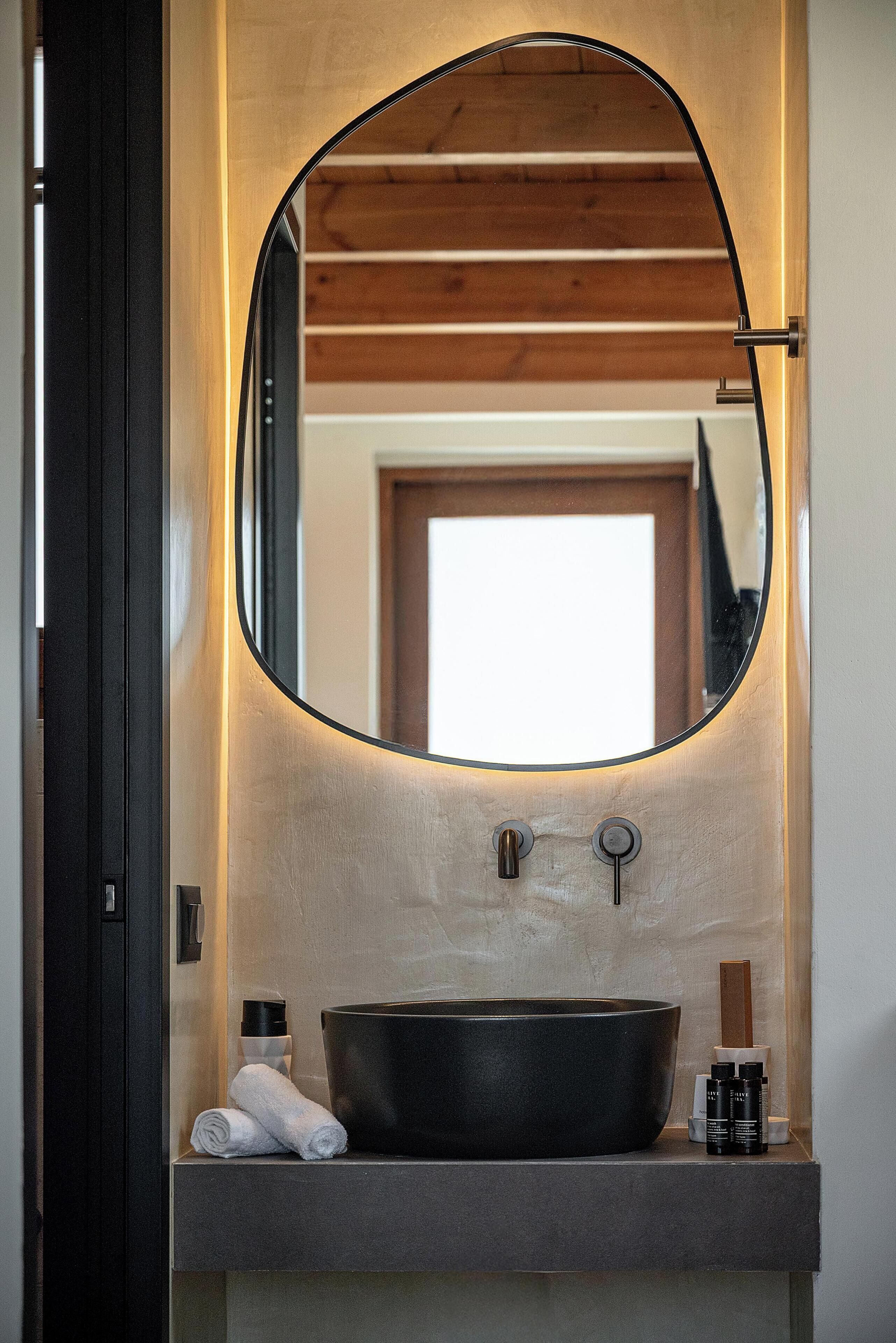 A bathroom with a round mirror, a black sink, and a wooden ceiling.