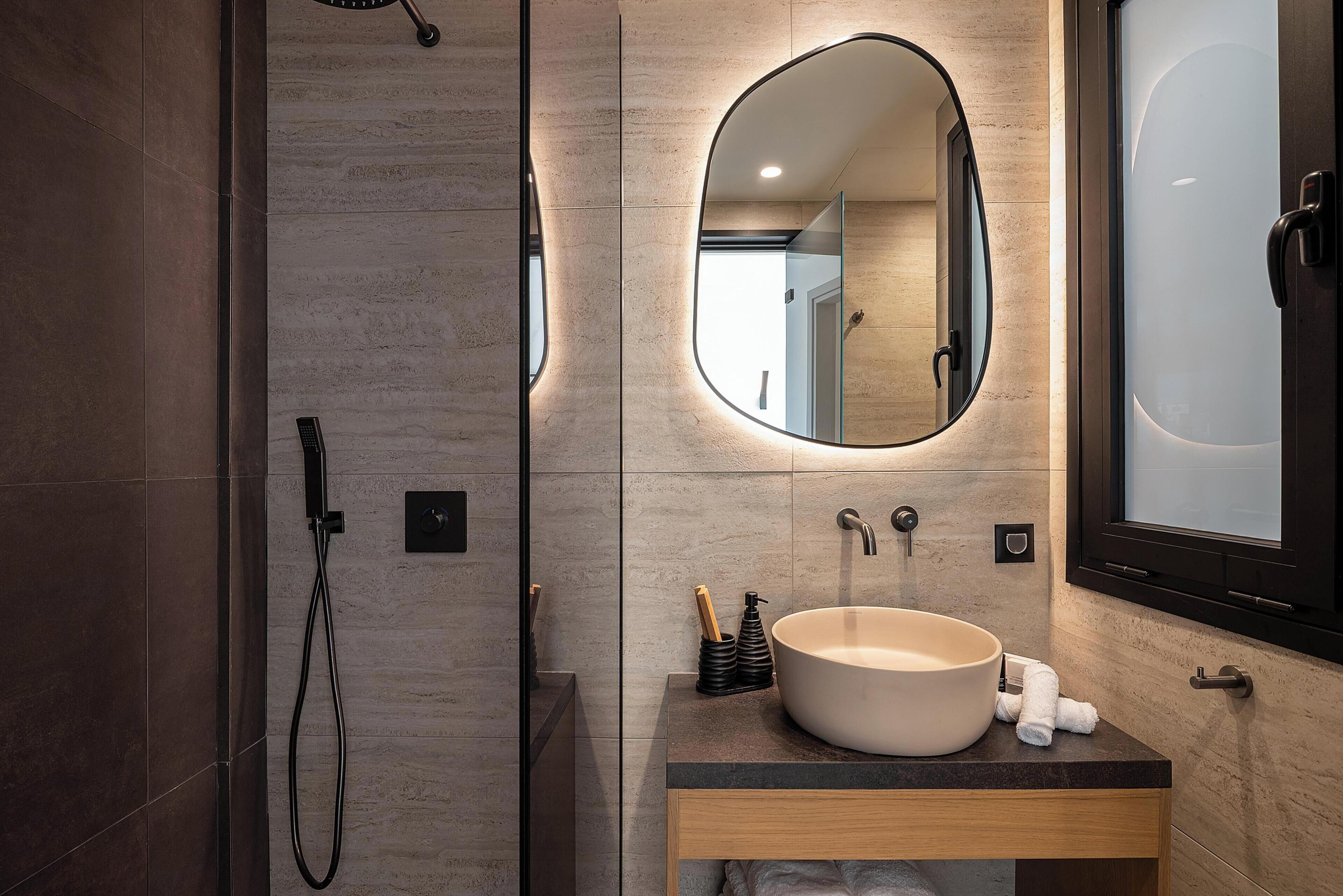 A modern bathroom with a large oval mirror, a round sink, and a shower area.