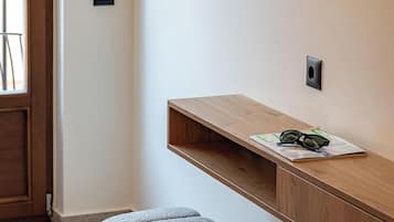 A modern room with a wooden bench, a round ottoman, a mounted TV, and a door leading to another space.